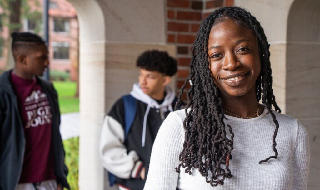 A student smiles at the camera with two more students in the background
