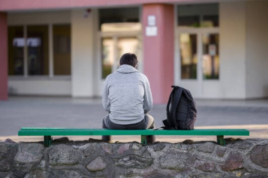 Stock image of a student sitting on a bench next to a backpack